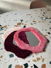 Fluffy multi-coloured yarn wrapping individual mirrors on a mosaic table.