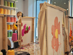 Girl in a ponytail creating a rug that contains a cherry pattern by using a tufting gun and colorful yarn in a colorful studio.